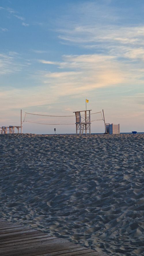 Free A peaceful beach scene at sunset featuring a lifeguard tower and volleyball net under a colorful sky. Stock Photo