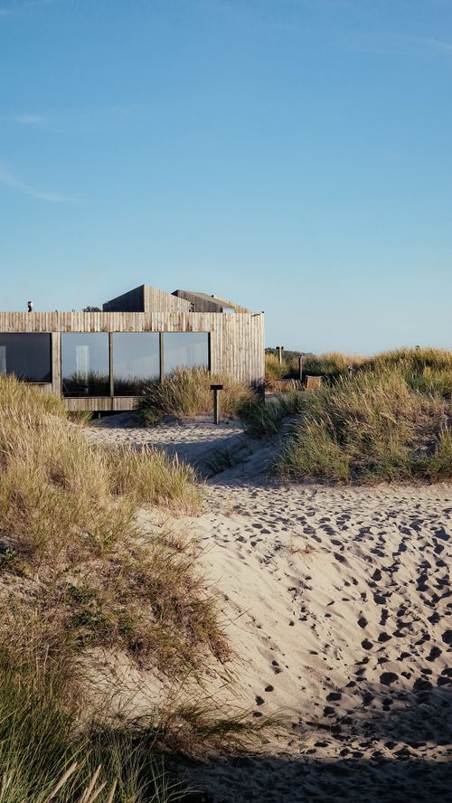 Free A modern wooden house sits peacefully amidst sandy dunes under clear skies. Stock Photo