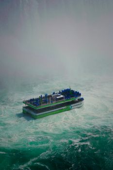 Tourist boat navigates misty waters of Niagara Falls, offering a thrilling view of the iconic landmark.