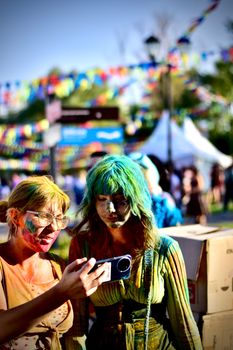 Two young women covered in vibrant colors enjoying a festive outdoor event.