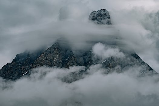 A dramatic photograph of a mountain peak enveloped in mist and clouds, creating a moody atmosphere.