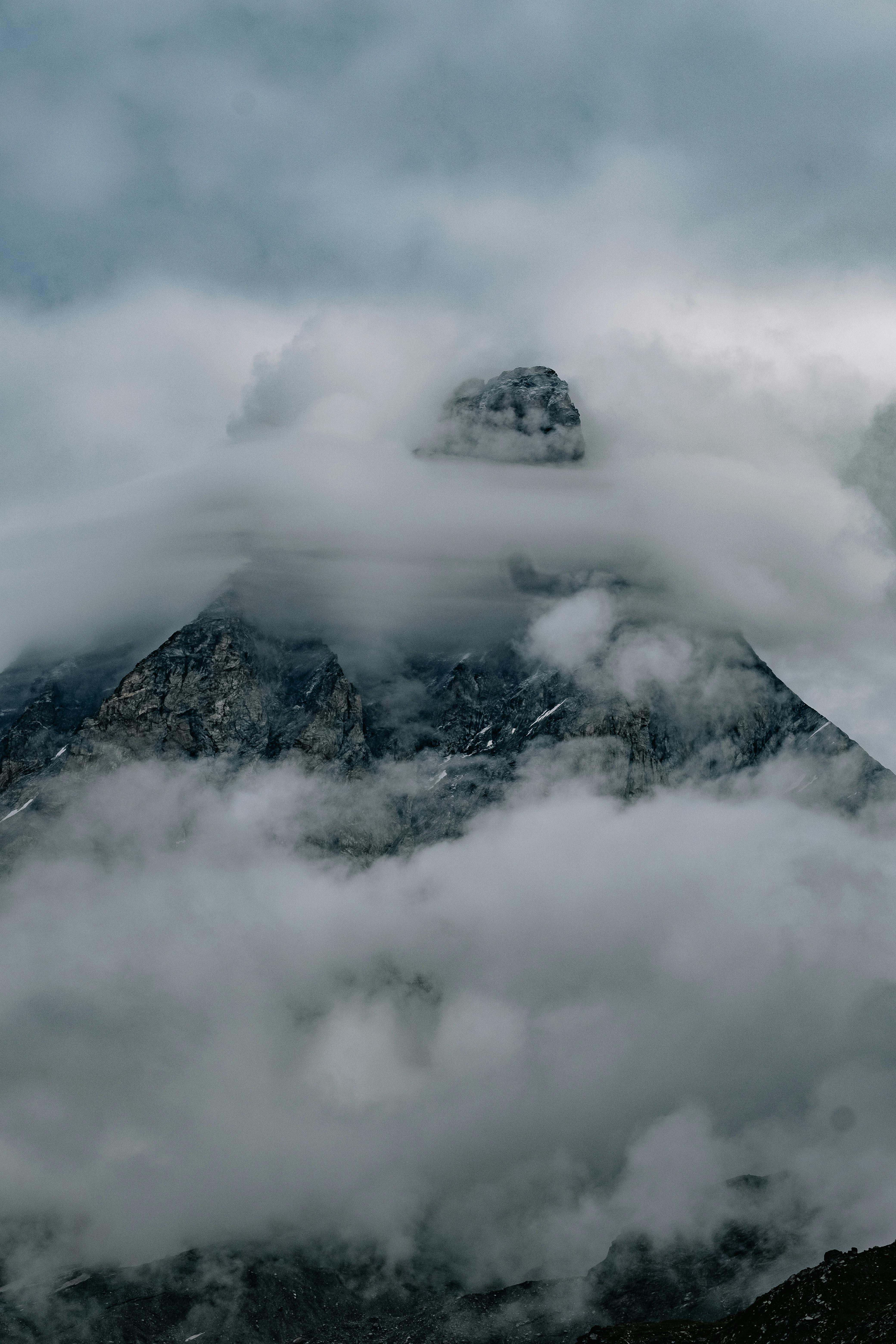A breathtaking view of a mountain peak wrapped in swirling mist and clouds, evoking a sense of mystery.