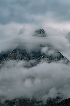 A breathtaking view of a mountain peak wrapped in swirling mist and clouds, evoking a sense of mystery.