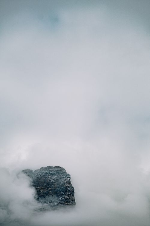 Free A mysterious mountain peak emerges through dense fog and clouds, creating a tranquil winter landscape. Stock Photo