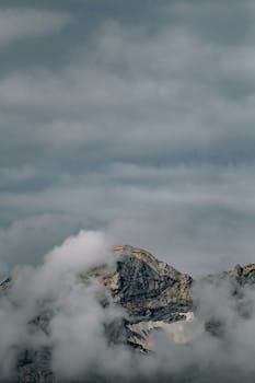 A rugged mountain peak shrouded in mist and clouds under a moody sky.