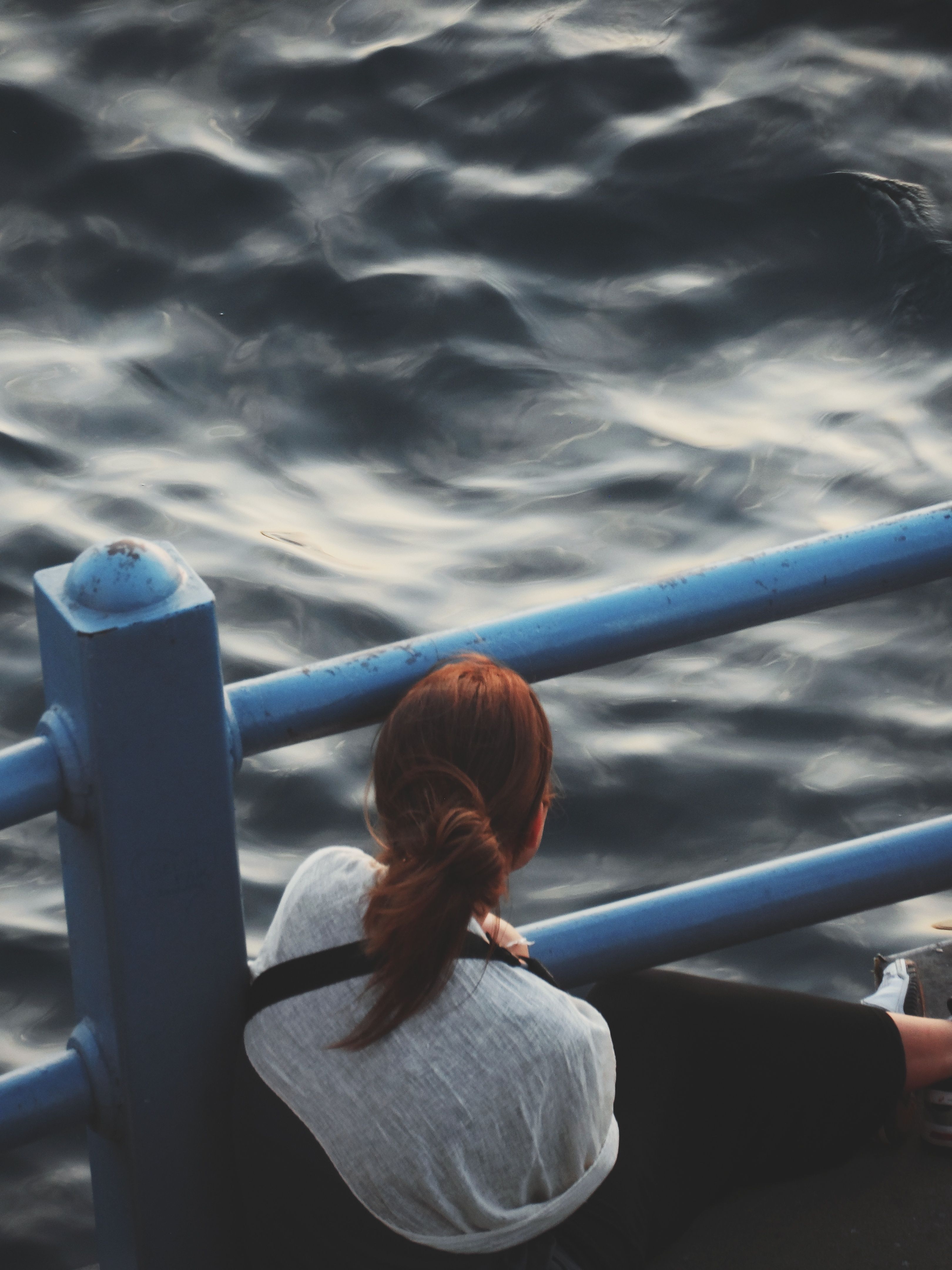 A woman sitting on a railing looking out over the water · Free Stock Photo