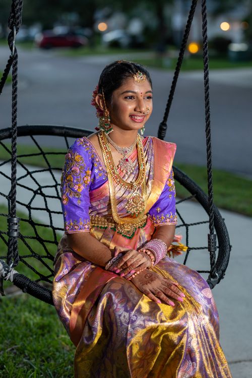 Free Portrait of a smiling young woman in traditional festive attire, sitting on a swing bench outdoors. Stock Photo