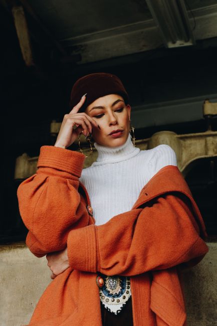 Fashionable woman in an orange coat and white turtleneck posing confidently outdoors.