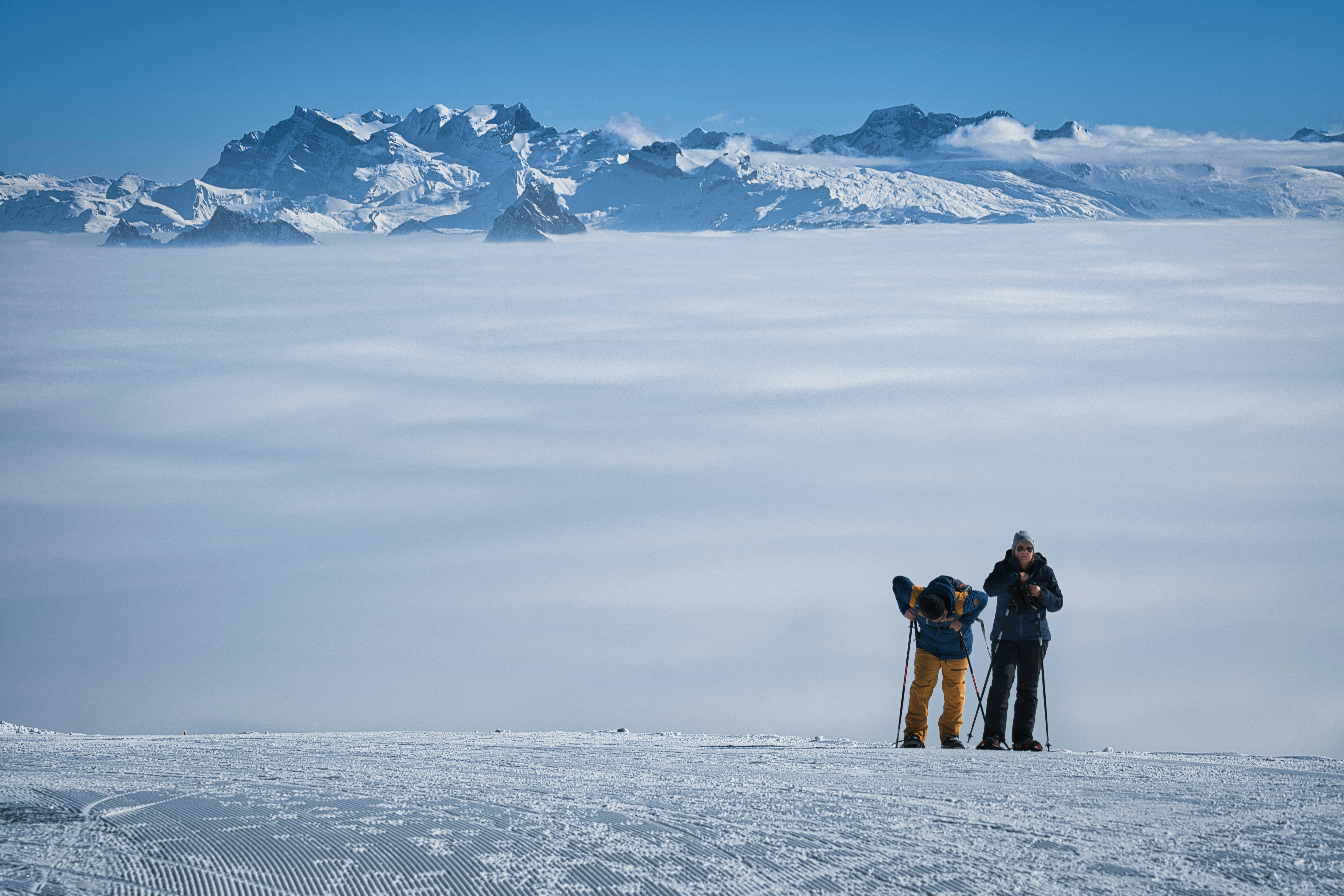 Two skiers preparing on a snow-covered slope with breathtaking mountain views and a sea of clouds.