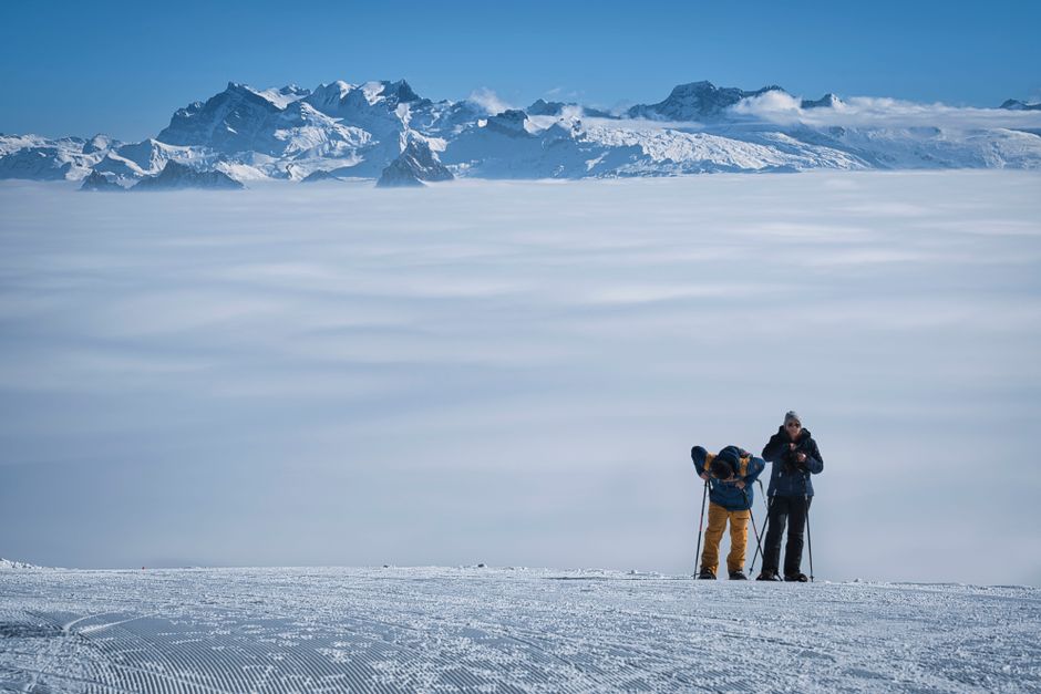Two skiers preparing on a snow-covered slope with breathtaking mountain views and a sea of clouds.