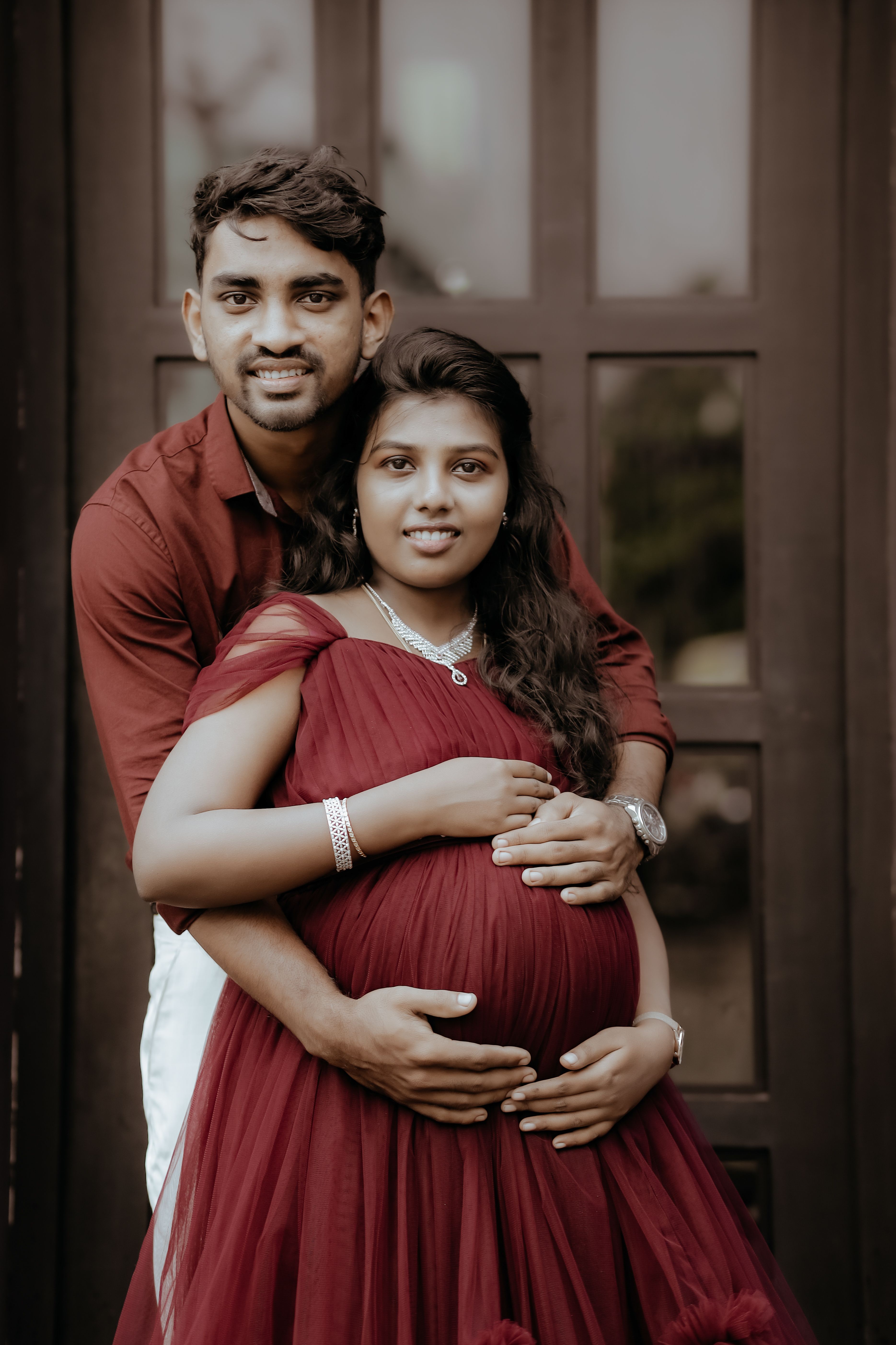 A happy couple joyfully embraces during pregnancy in an indoor setting.