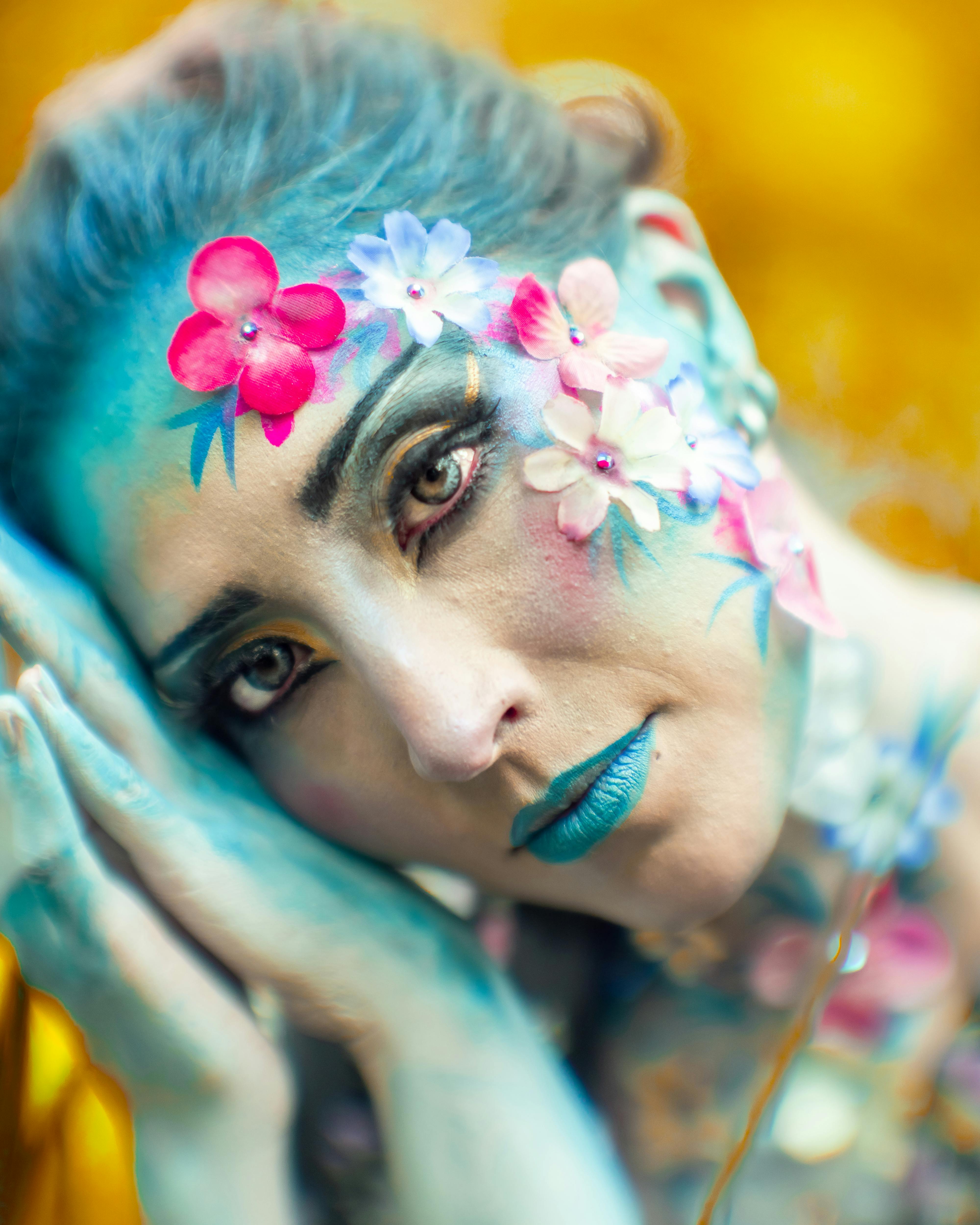 Artistic portrait of a woman in blue with floral makeup, evoking a fantasy.