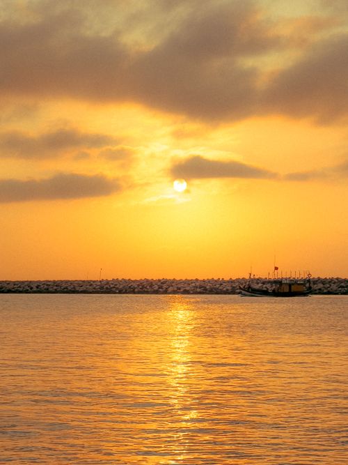 Free Serene sunset view with golden reflections over the ocean and silhouetted boat. Stock Photo