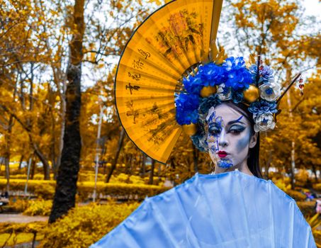 A vibrant geisha-inspired character with ornate headpiece poses outdoors in Mexico City.