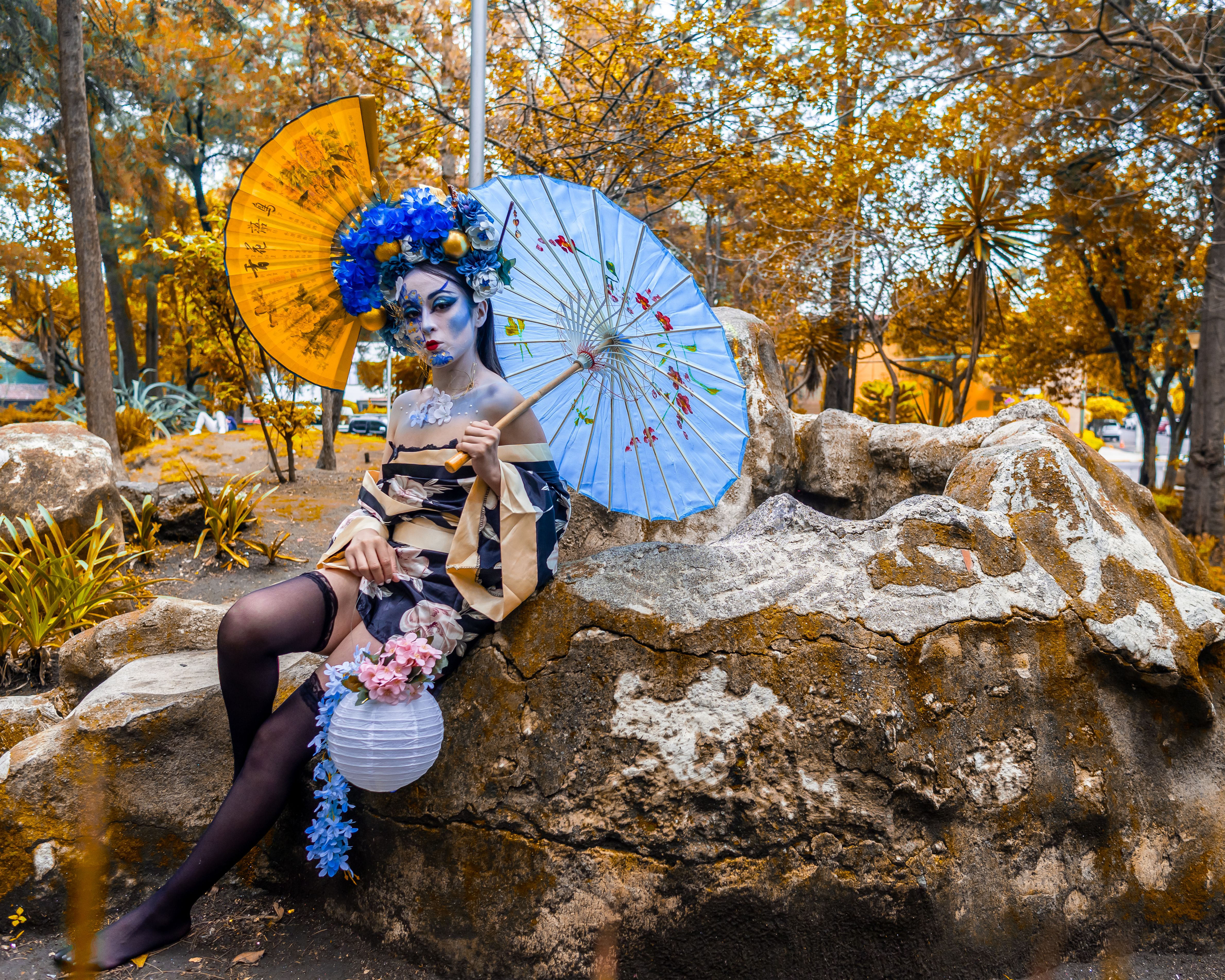 Person in traditional costume with makeup and parasol in a park setting.