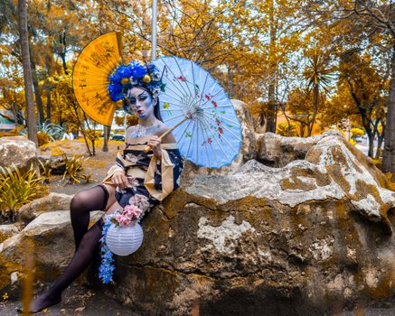 Person in traditional costume with makeup and parasol in a park setting.