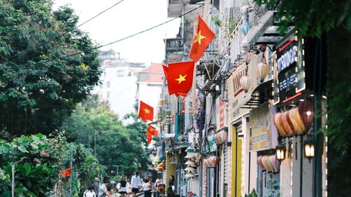 Free Vibrant street view in Vietnam with red flags, shops, and people walking by. Stock Photo