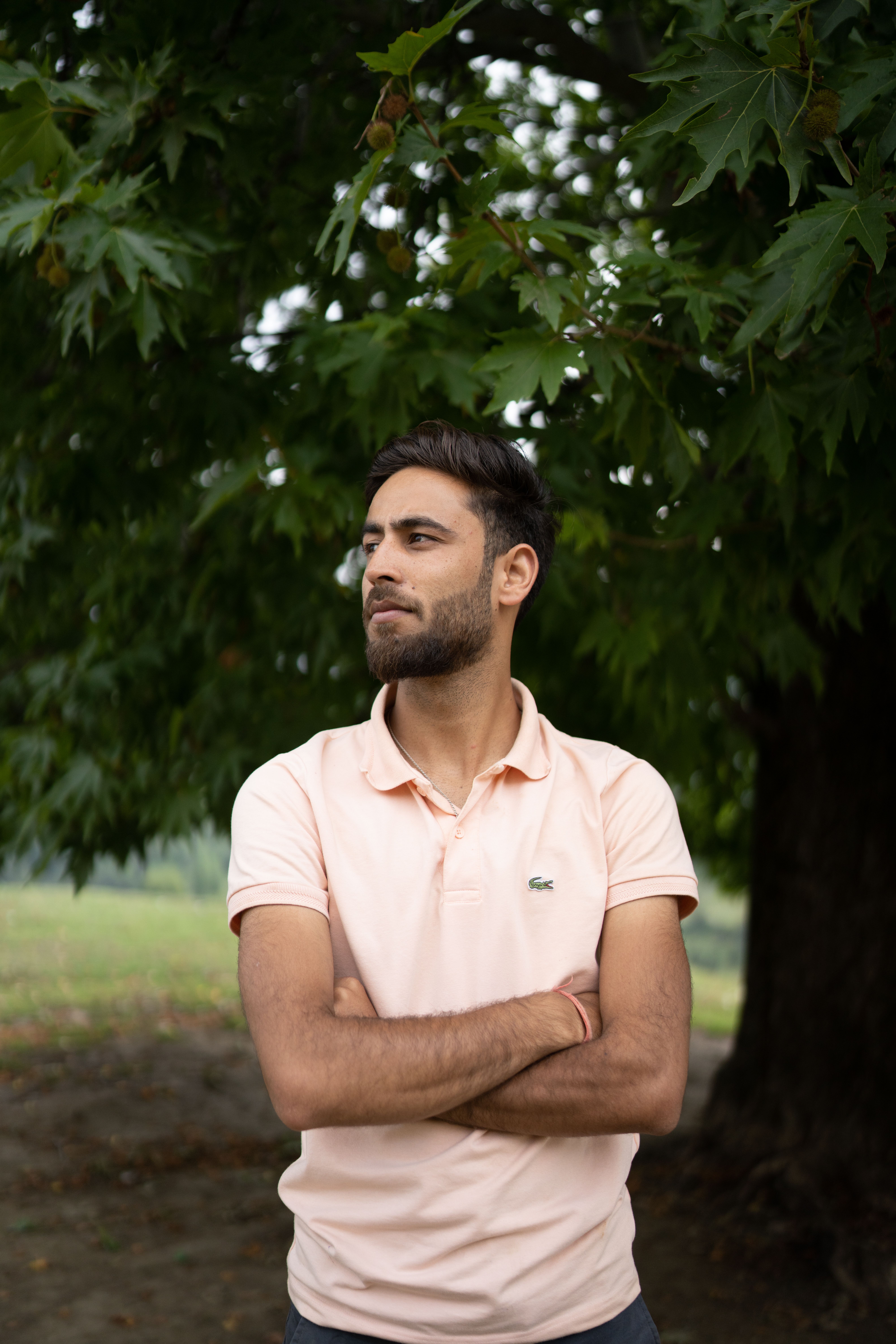 Portrait of a bearded man in a pink polo shirt with arms crossed, posed outdoors in the lush Srinagar countryside.