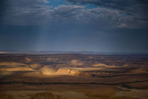 Free A breathtaking aerial view of a desert canyon landscape with dramatic clouds and sunlight penetration. Stock Photo