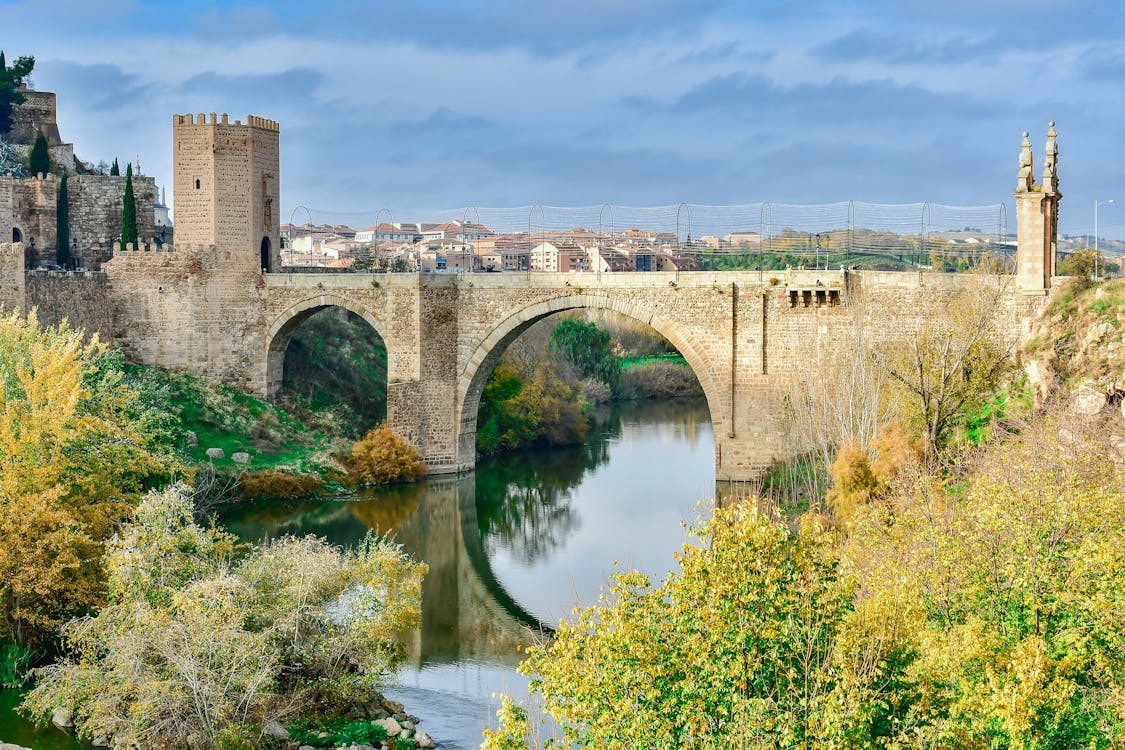 Free Historic Puente de San Martín arches over the river in Toledo, surrounded by lush autumnal scenery. Stock Photo