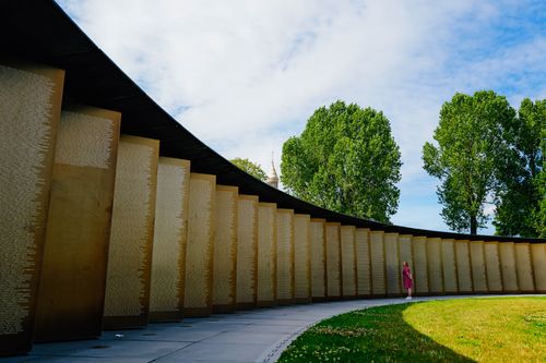 Free A solitary figure in red stands near a modern curved monument wall on a sunny day with trees. Stock Photo