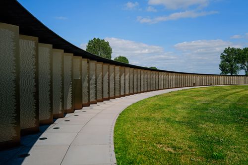 Free A curved memorial wall under a clear blue sky in a sunlit park with grassy surroundings. Stock Photo