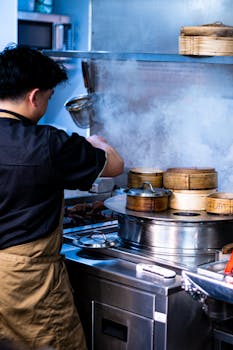 Chef cooking Asian dim sum in a busy restaurant kitchen with steam rising.