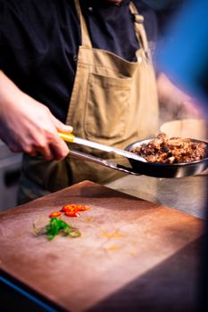 Close-up of a chef using tongs to prepare a dish in a kitchen setting.