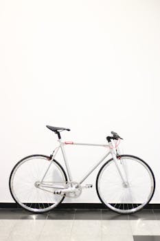 Modern silver bicycle stands elegantly against a white wall. Ideal for urban lifestyle themes.