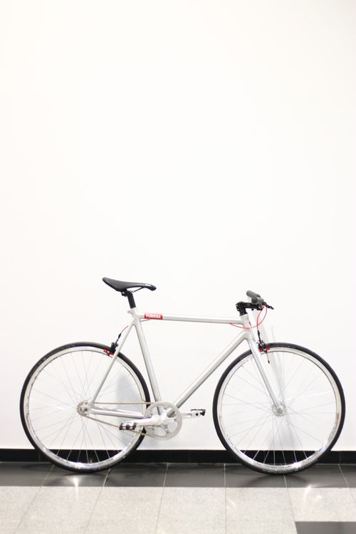 Free Modern silver bicycle stands elegantly against a white wall. Ideal for urban lifestyle themes. Stock Photo