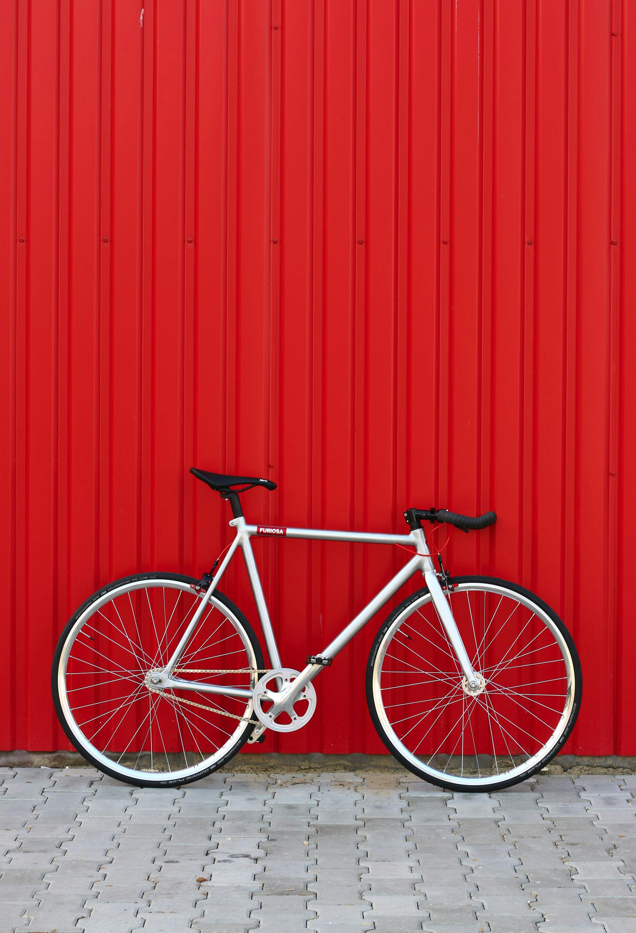 Sleek white bicycle leaning on a vibrant red wall, showcasing minimalist design.
