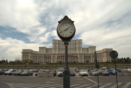 View of the Bucharest Parliament Palace with iconic street clock and cloudy sky.