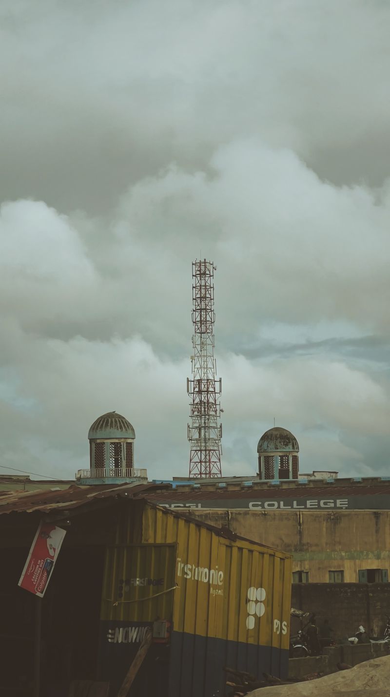 A towering antenna amidst industrial buildings and cloudy skies in Kaduna, Nigeria.