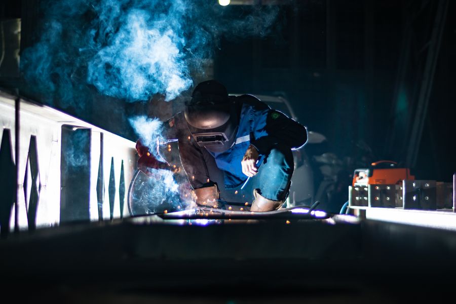 Welder in protective gear joining steel with bright sparks indoors