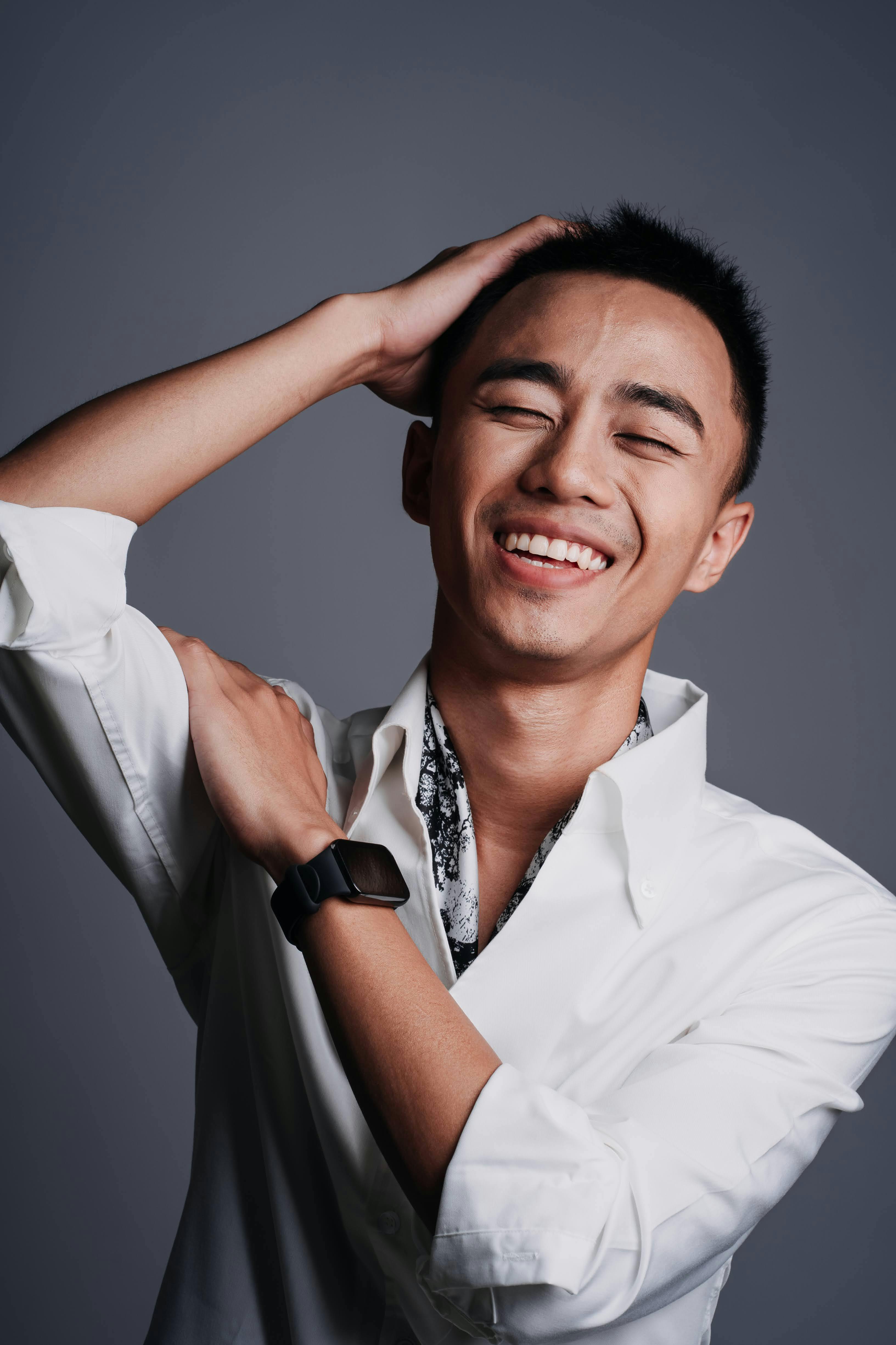 A cheerful young man with eyes closed, posing in a white shirt inside a studio.
