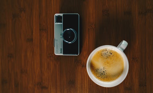 Taza De Cerámica Blanca Al Lado De Una Cámara Negra Y Gris