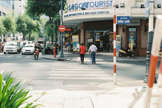 Busy intersection in Ho Chi Minh City with pedestrians crossing and Saigontourist building.