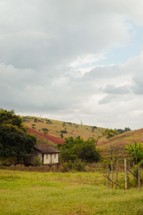 Free Serene rural scene featuring a solitary cottage amidst rolling hills under a cloudy sky. Stock Photo