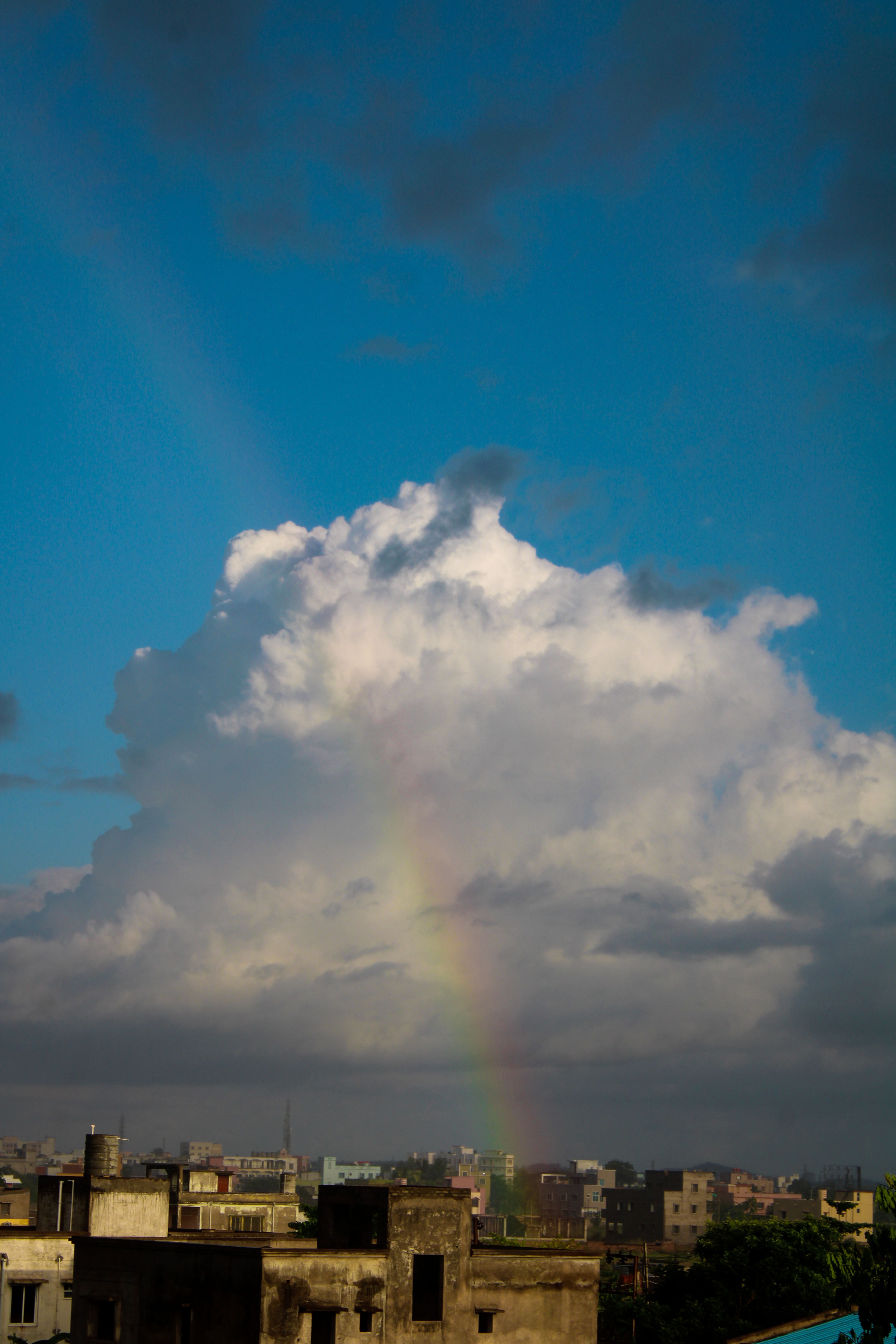 Vibrant rainbow arches across cloudy sky over urban rooftops in Odisha, India. Stunning weather scene.