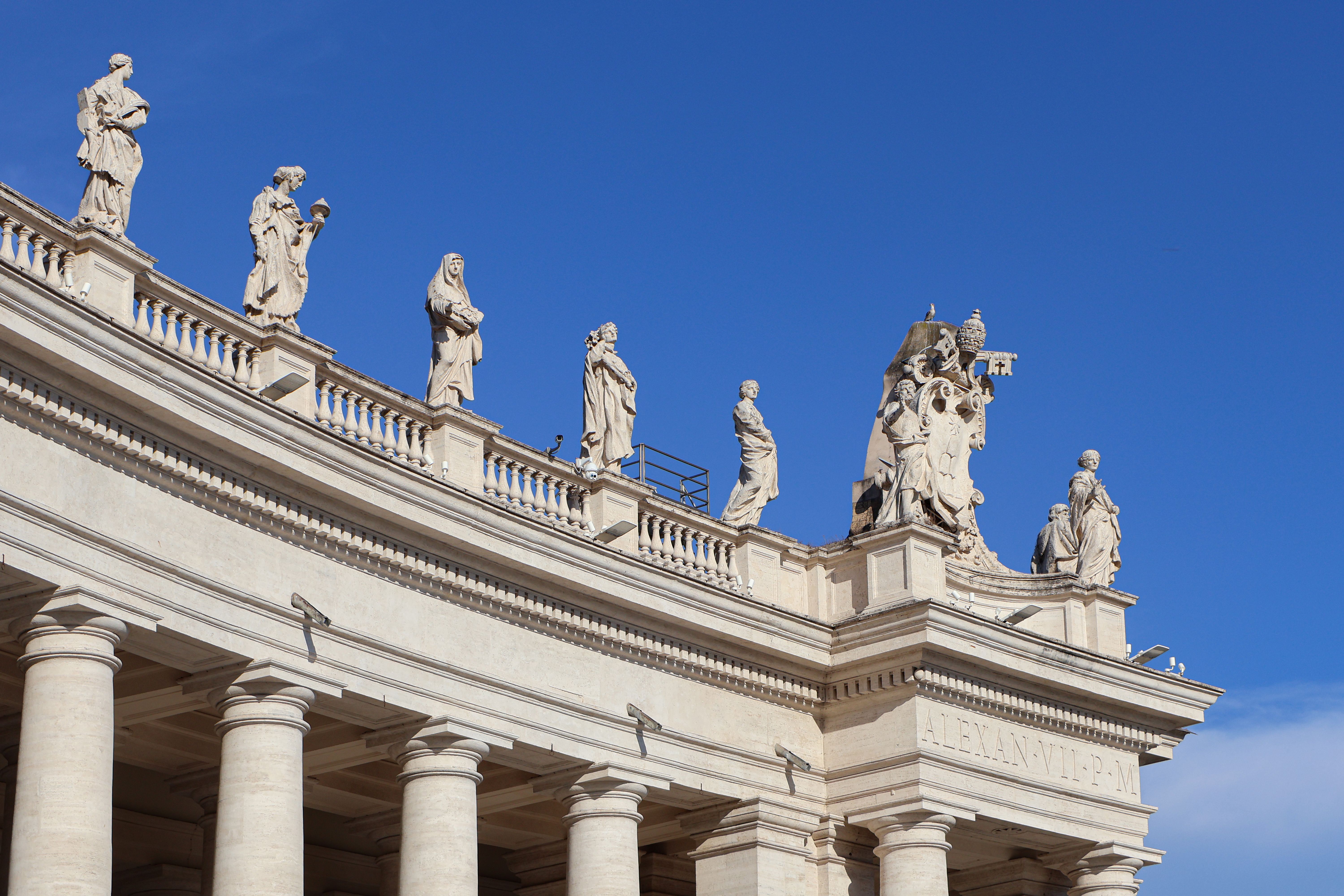 Detailed view of sculptures on Saint Peter's Basilica, Vatican City, under a clear blue sky.