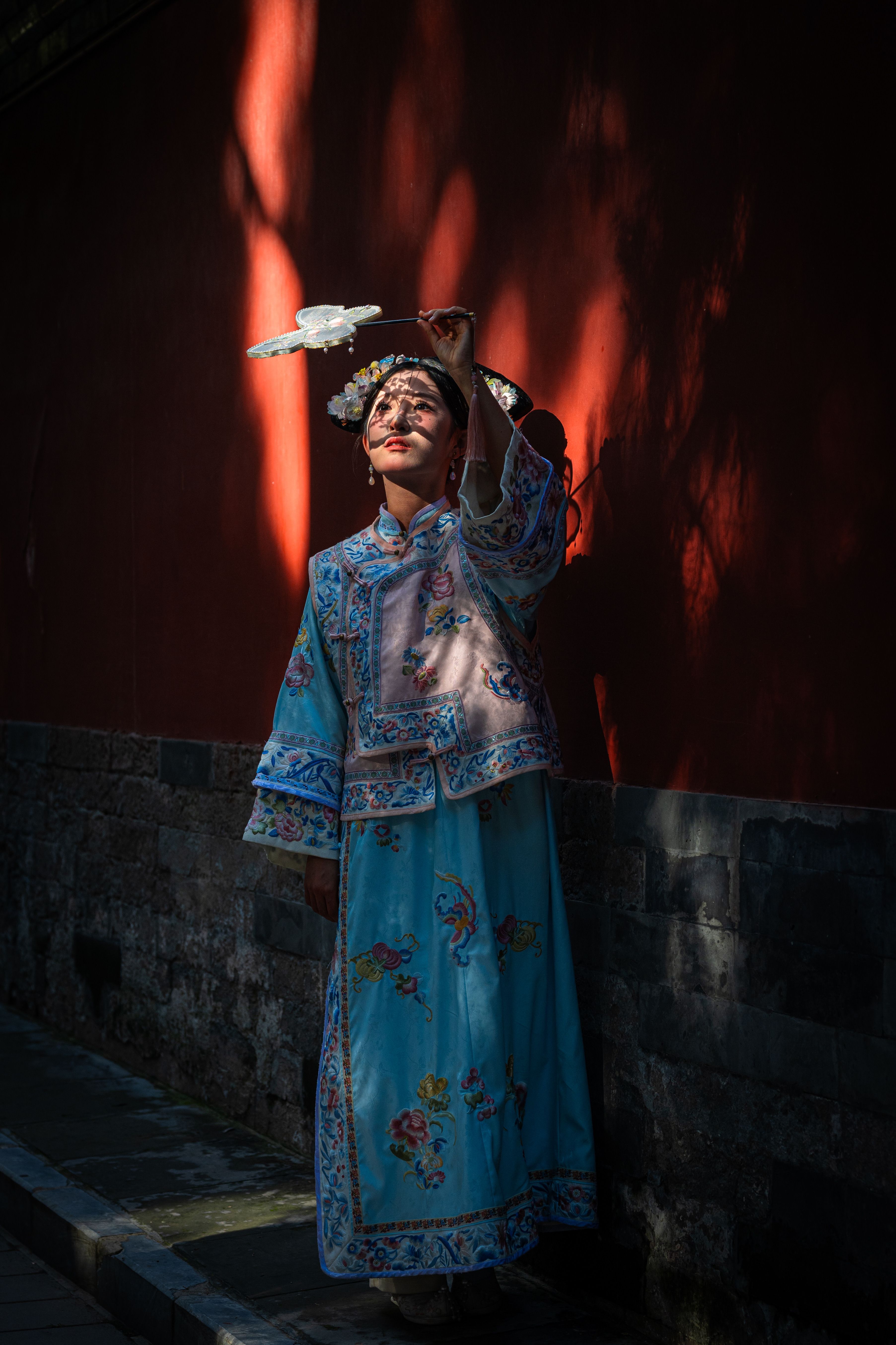 A person in traditional Asian costume poses dramatically against a shaded wall, invoking cultural artistry.