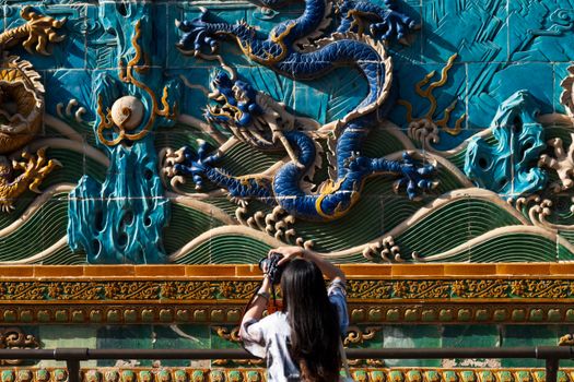 A woman photographs a vibrant dragon wall, showcasing intricate traditional art.