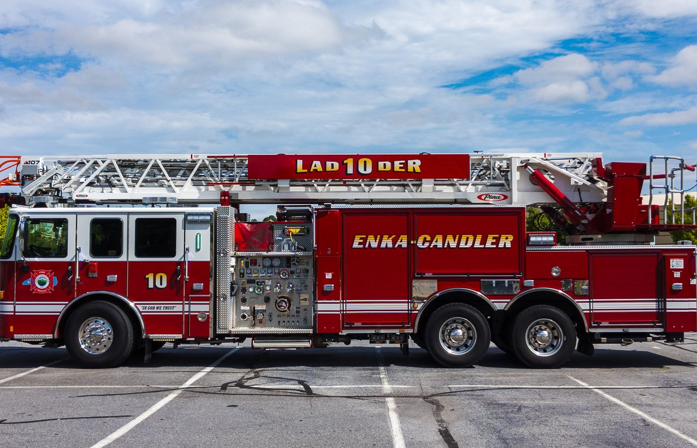 Side view of a red fire truck in an outdoor parking lot under a bright sky.