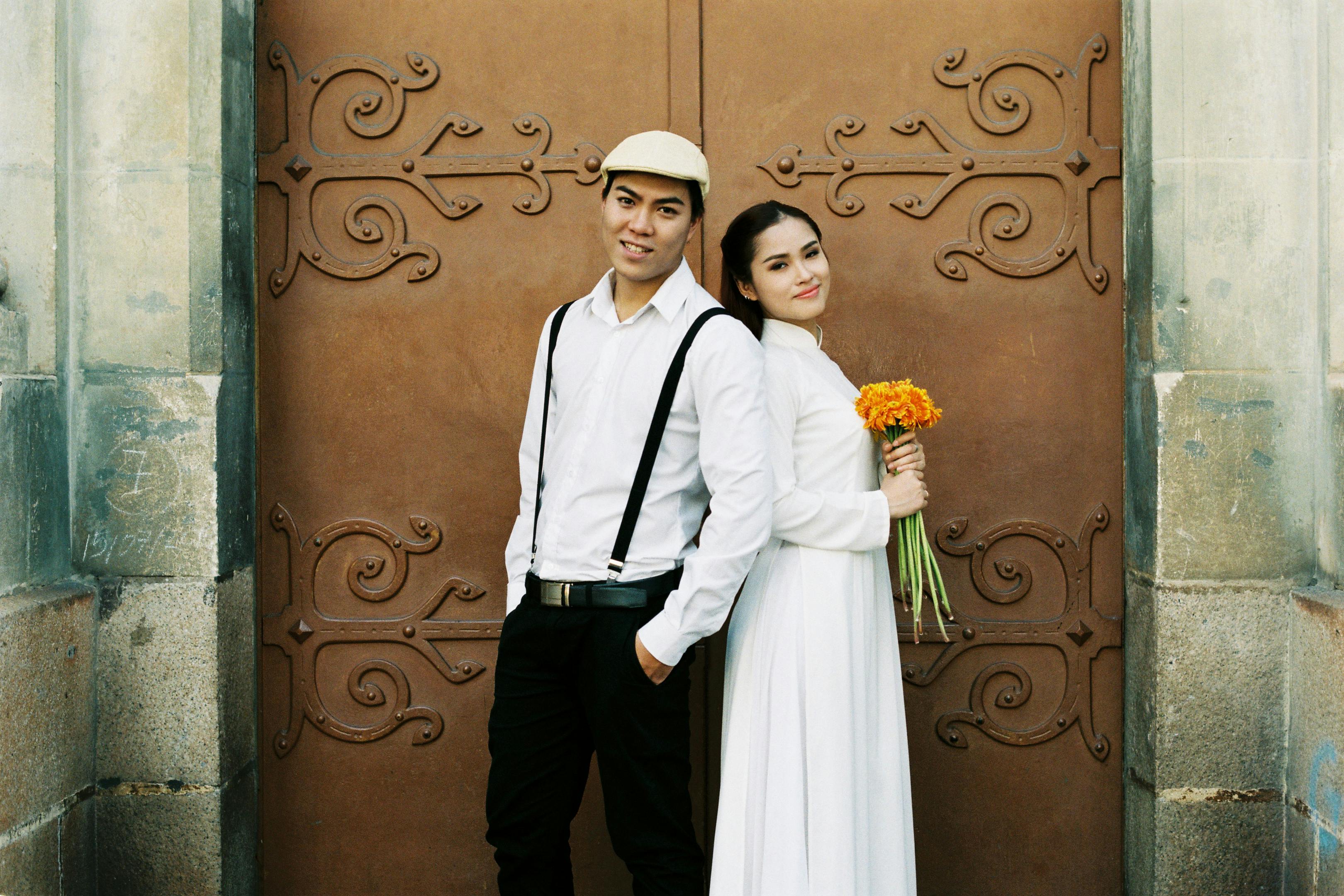 Couple in traditional Vietnamese attire posing by an ornate gate in Ho Chi Minh City.