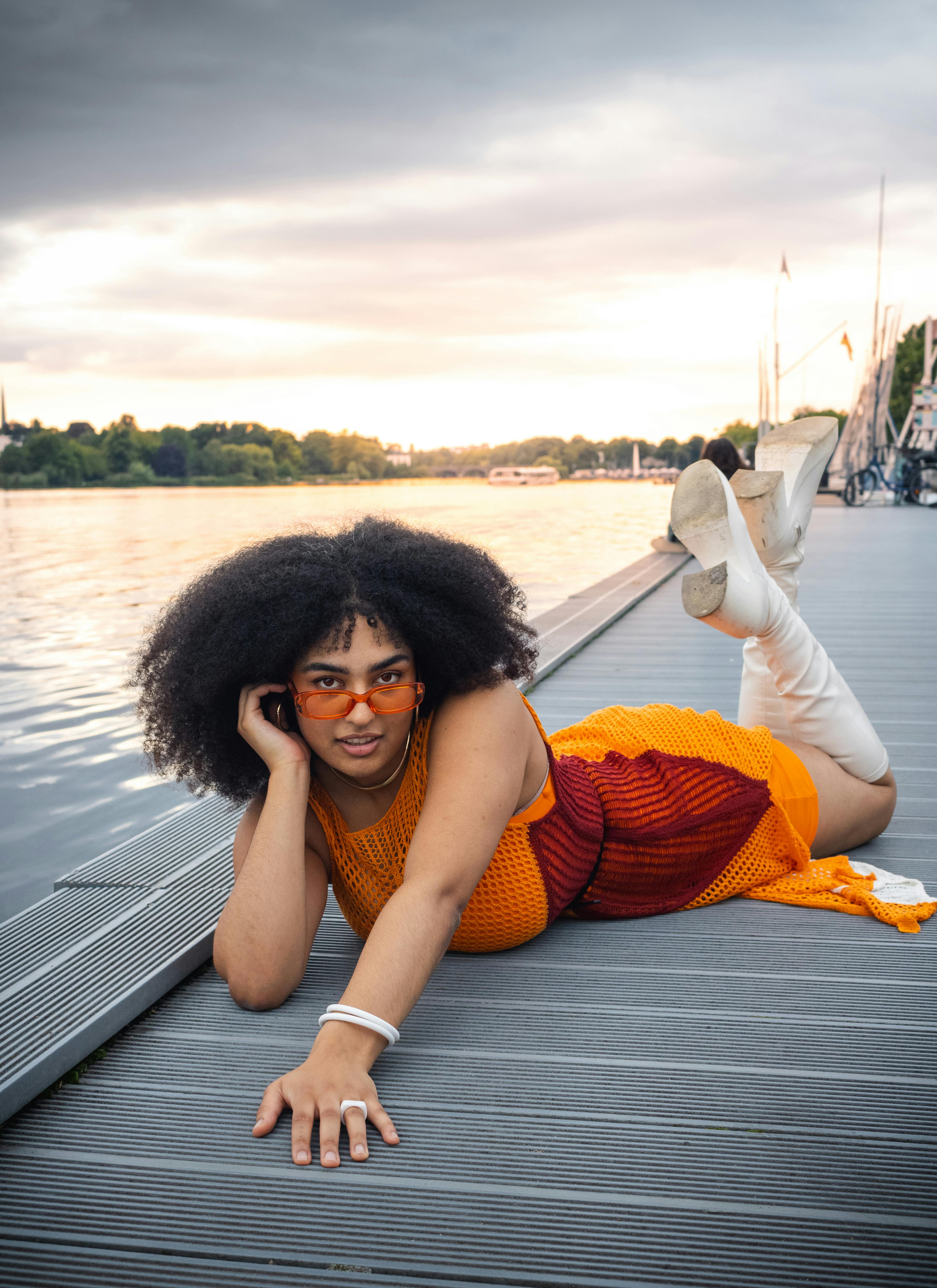 a woman in sunglasses and an orange dress is laying on a dock