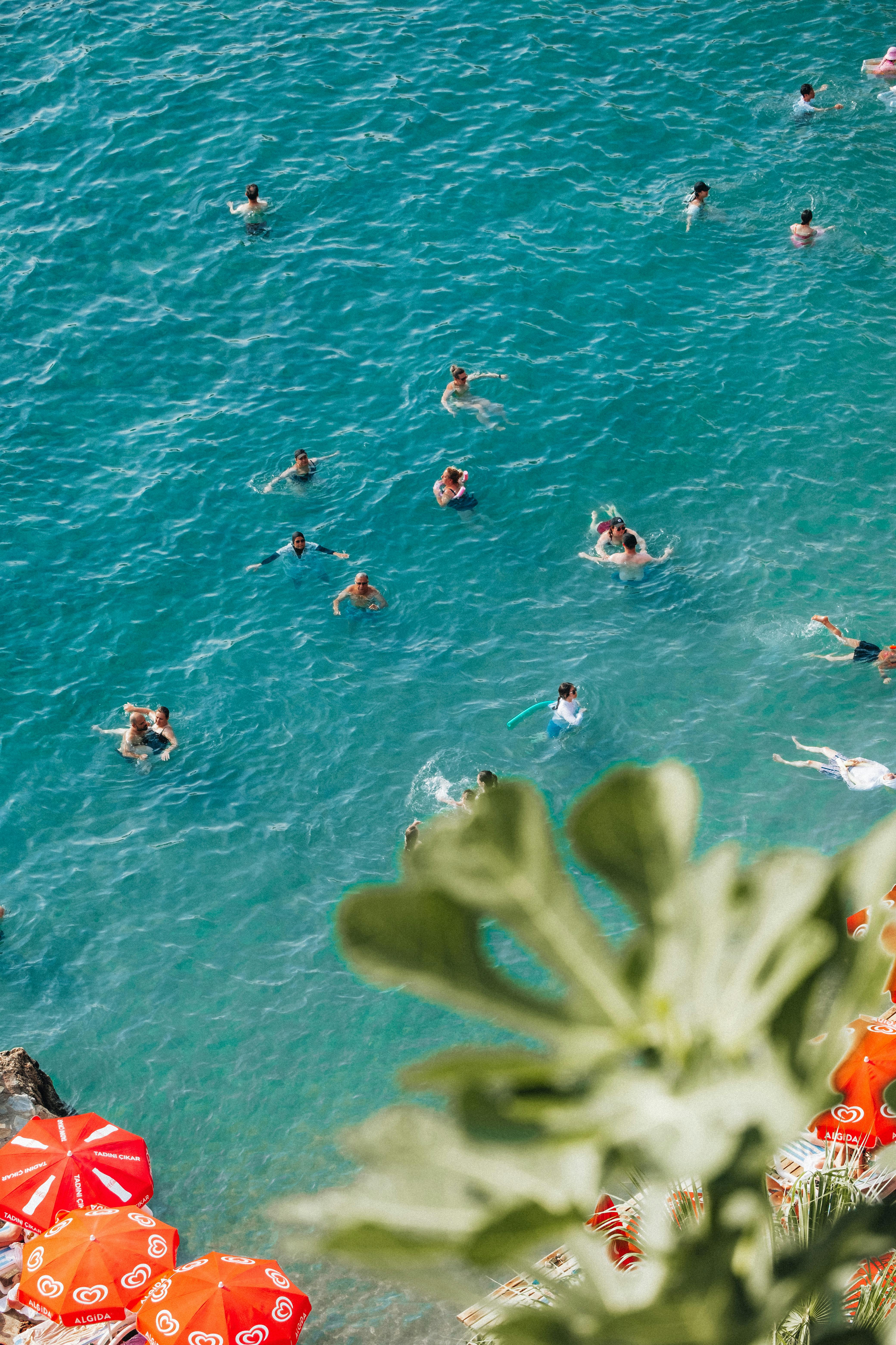 Swimmers enjoying clear turquoise waters from a high angle with vibrant red umbrellas.