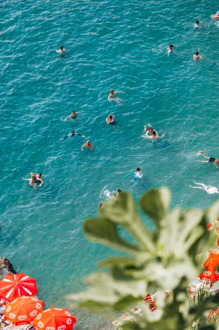 Swimmers enjoying clear turquoise waters from a high angle with vibrant red umbrellas.