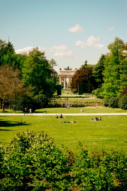 People enjoying a sunny day at Parco Sempione, Milan with the Arch of Peace visible.