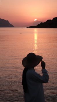 Silhouette of a person with hat at sunset, reflecting on calm sea.