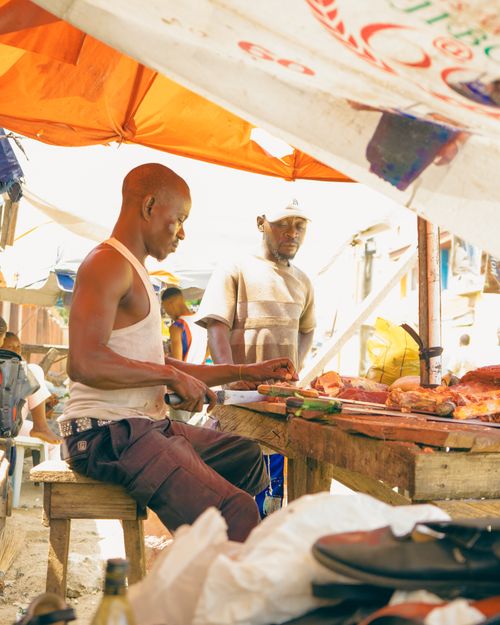 Free A candid shot of a man preparing food at an outdoor market stall under a vibrant canopy. Stock Photo